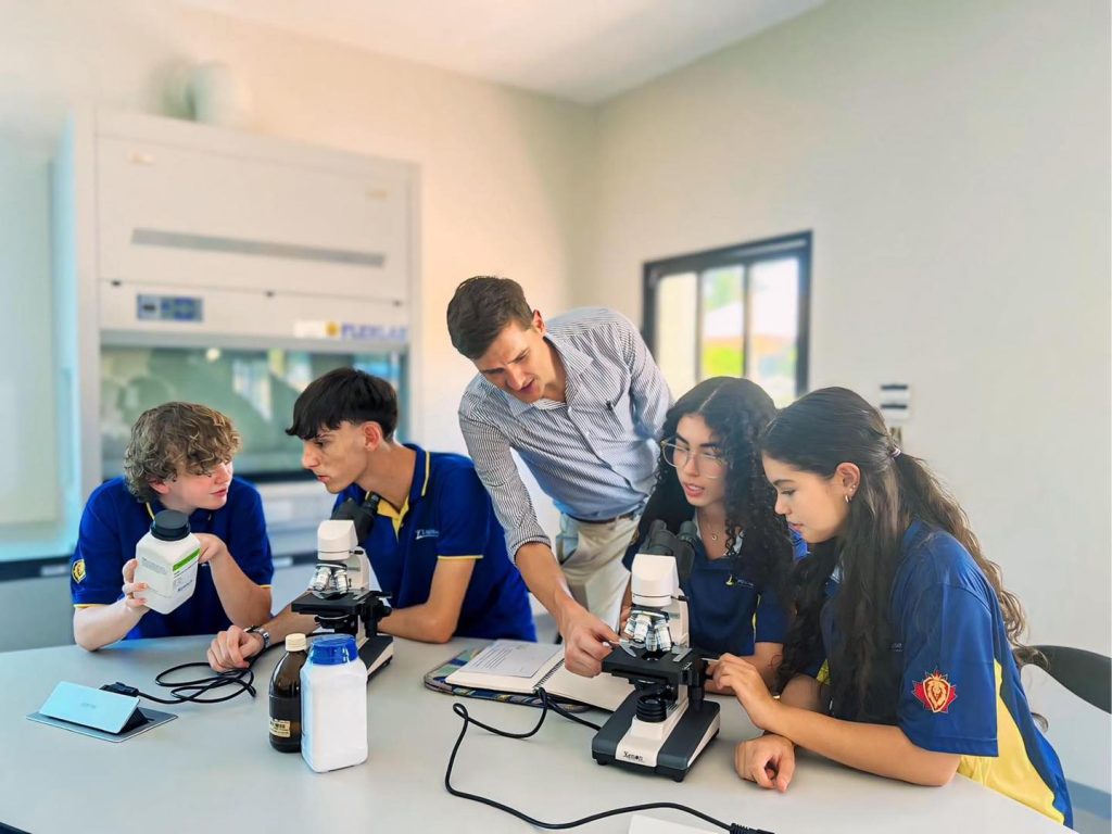 Secondary school students looking at microscope equipment and being assisted by their teacher