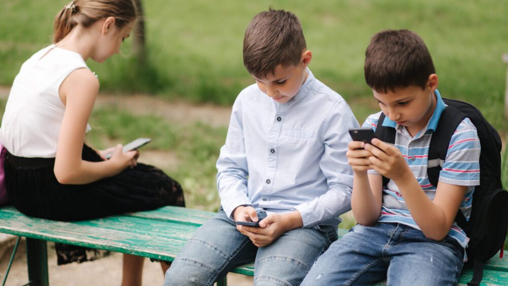 two boys and girl use their phones during school break