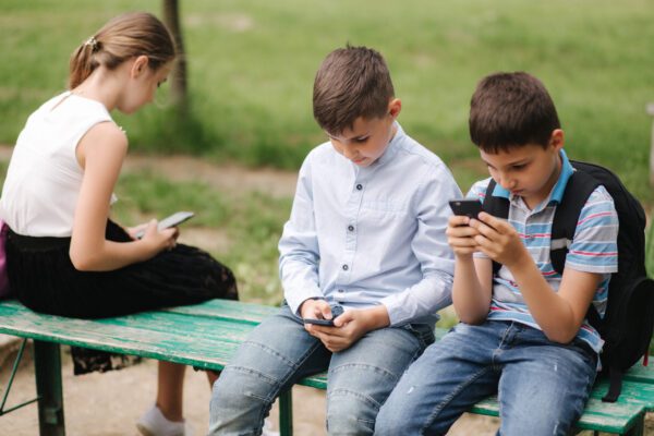 two boys and girl use their phones during school break