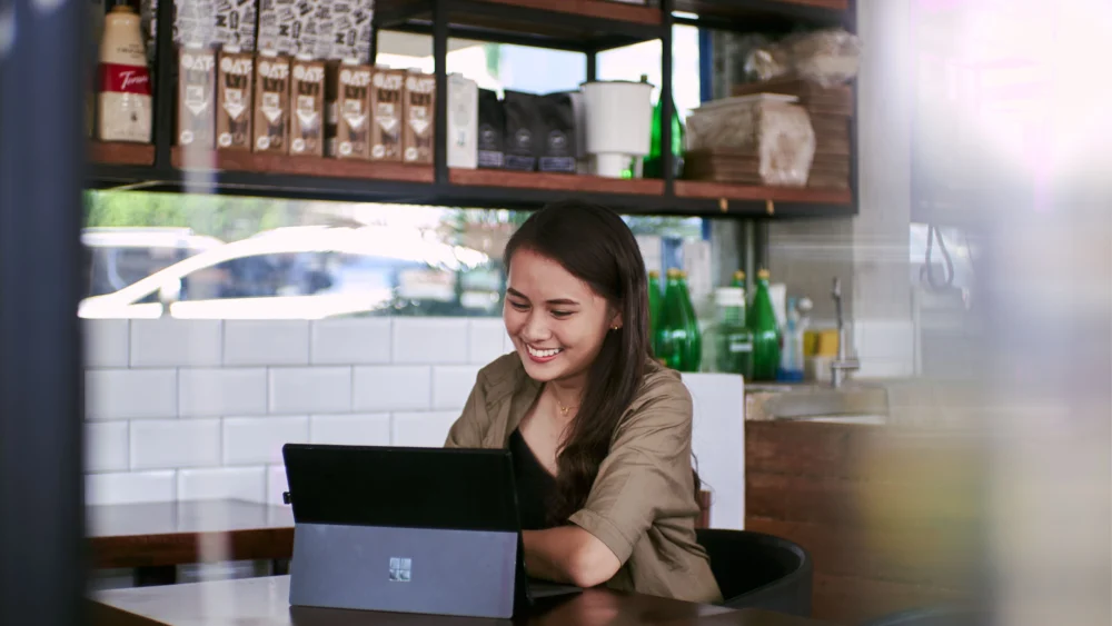 A woman in a cafe smiling while working on a tablet
