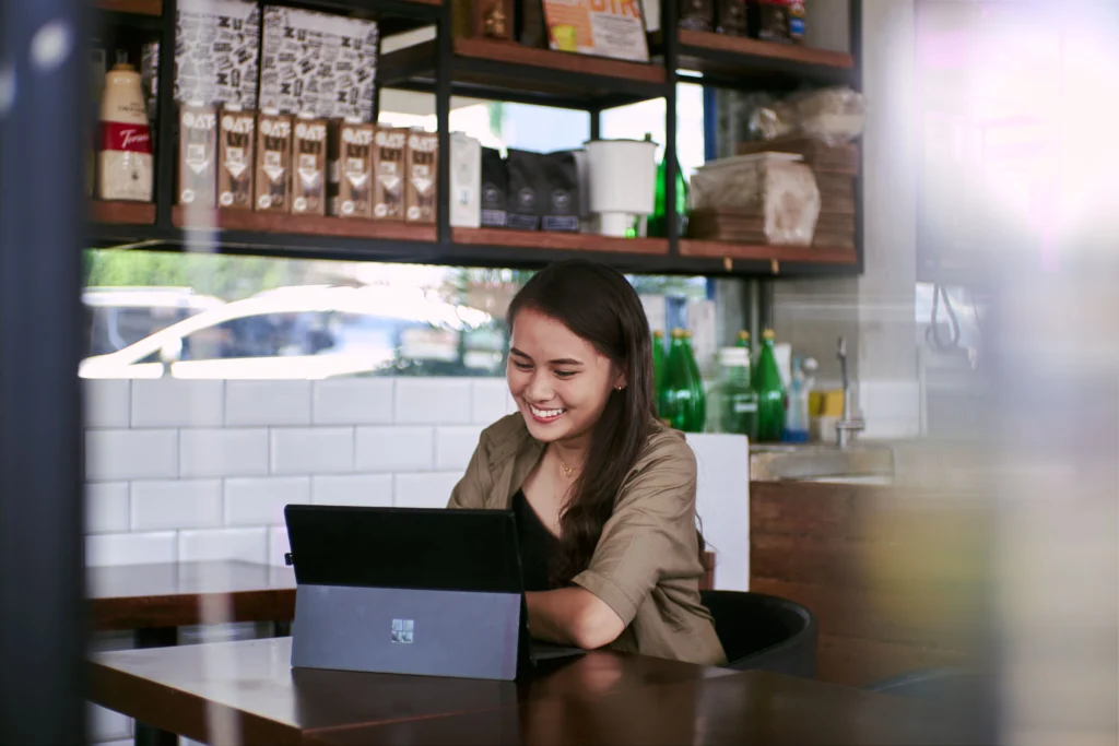 A woman in a cafe smiling while working on a tablet
