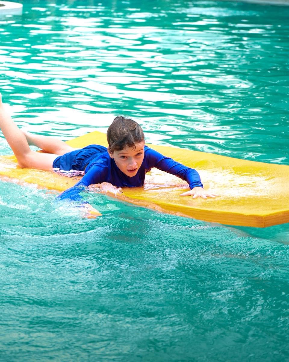 Lighthouse International School Student paddling with a board in the pool at YouTopia Phuket summer camp Lighthouse International School Student paddling with a board in the pool at YouTopia Phuket summer camp