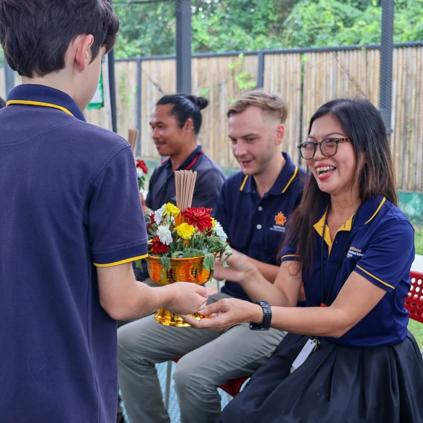 A Lighthouse student handing the teacher a flower arrangement for Wai Kru Day